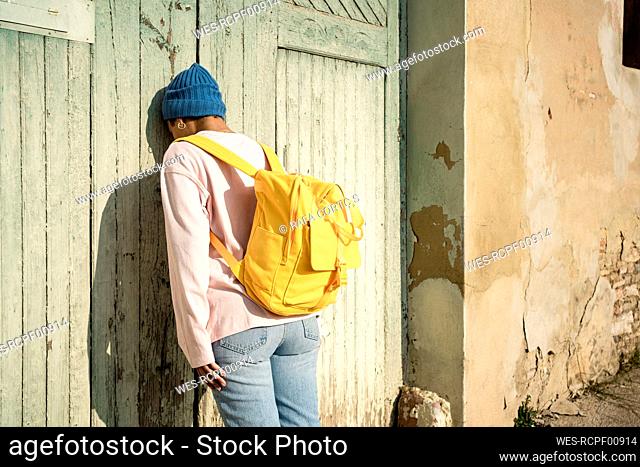 Lonely Woman wearing yellow backpack leaning on old wooden door