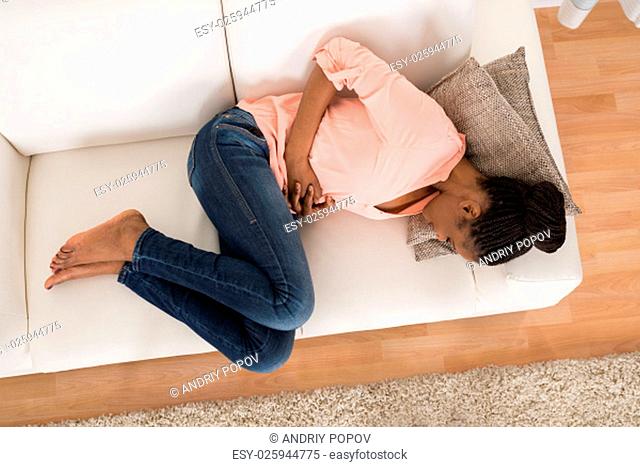 High Angle View Of Young African Woman With Stomach Ache Lying On Sofa