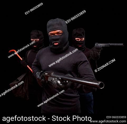 Closeup portrait of robber posing with rifle over black background with his partners. Studio shot of muscular men with weapons. Isolated on black