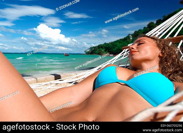 Young woman swinging in hummock on blue sea background