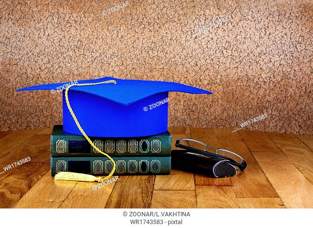 Graduation mortarboard on top of stack of books on abstract background of wall