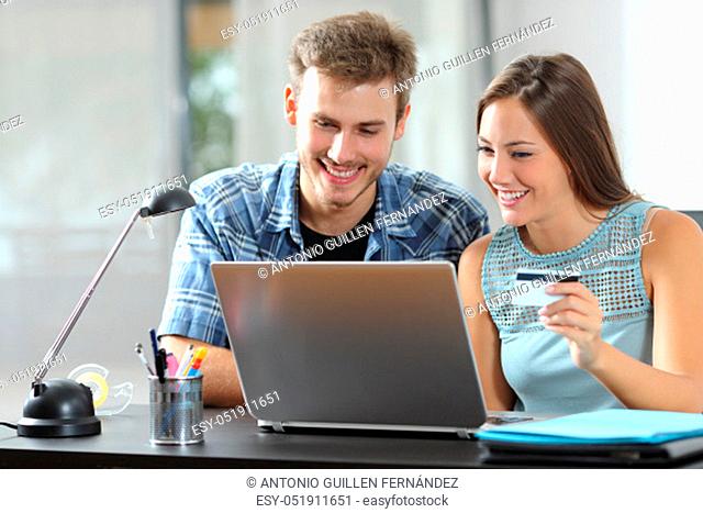Happy couple at home paying online with credit card and laptop on a desk in a room