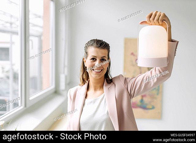 Portrait of smiling businesswoman holding lantern in office