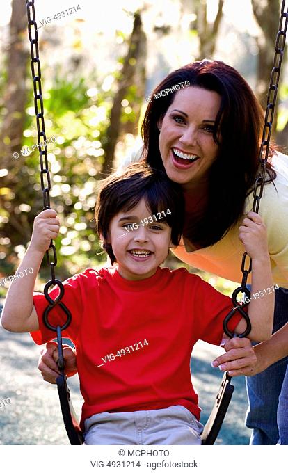 Hispanic mother and son having fun outdoors in park on swing and laughing - 31/03/2020