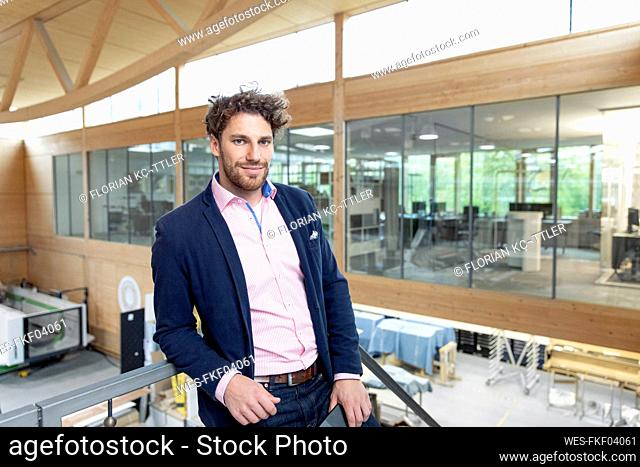 Young businessman leaning on railing at factory