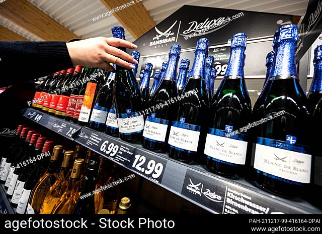 PRODUCTION - 15 December 2021, North Rhine-Westphalia, Kaarst: A woman takes a bottle of Blanc de Blancs from the shelf with Sansibar and deluxe products in a...
