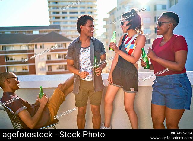 Happy young friends drinking beer on sunny urban rooftop balcony