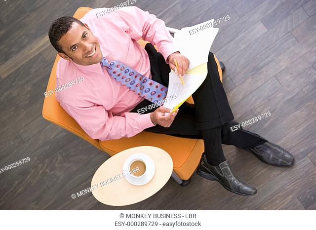 Businessman sitting indoors with coffee and folder smiling