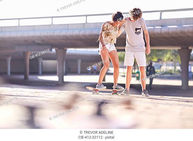 Teenage boy teaching girlfriend skateboarding at sunny skate park