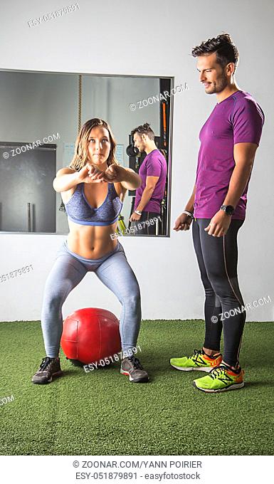 Young woman doing squat being supervise by coacb