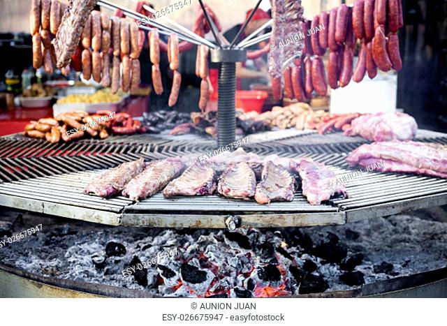 A huge circular grill loaded with assorted ribs, chorizos, chicken and others