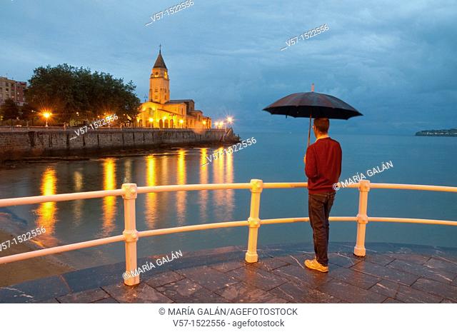 Man with umbrella on the promenade, night view. Gijón, Asturias province, Spain