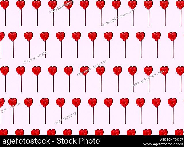 Pattern of heart shaped lollipops flat laid against pink background