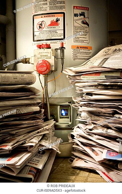 Piles of newspapers next to lit gas boiler