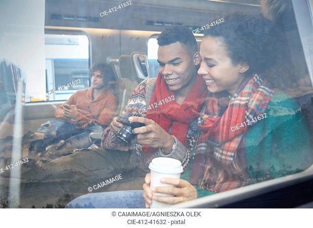 Young couple with coffee looking at digital camera at window on passenger train