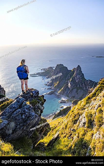 Evening sun, hiker standing on a rock, view of cliffs in the sea, top of the mountain Måtinden, near Stave, Nordland, Norway, Europe