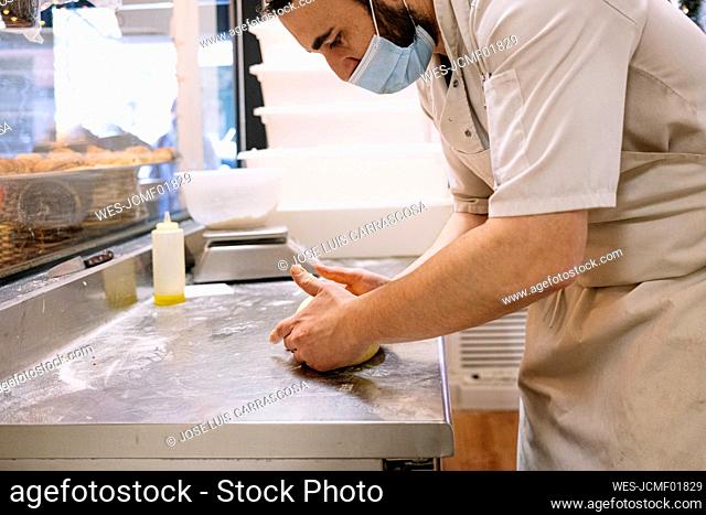 Mid adult male chef kneading bread dough on counter in commercial kitchen