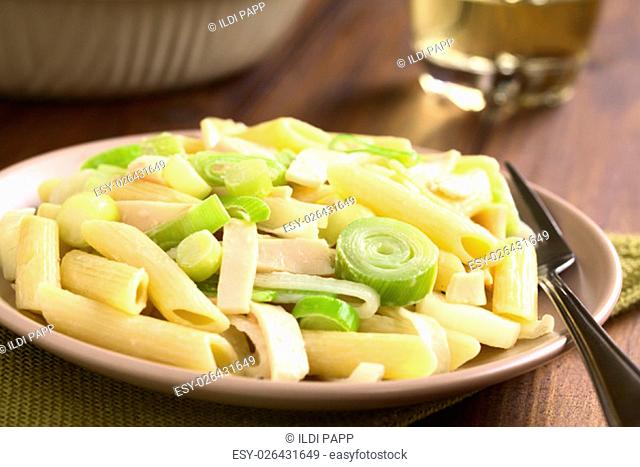 Pasta dish with ham and leek in cream sauce served on plate, photographed overhead on dark wood with natural light (Selective Focus