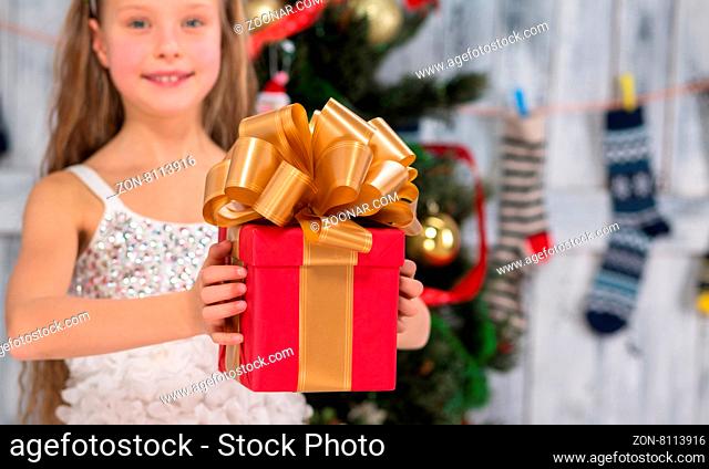 Close-up portrait of New Year and Christmas present with gold ribbon and bow. Little girl in white dress going to prepare it for someone