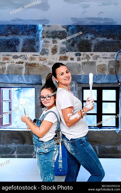 Portrait of mother and daughter posing with paintbrush and paint roller