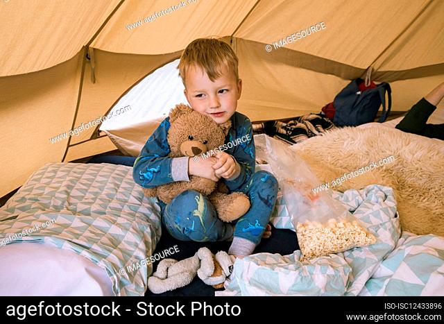 Boy (18-23 months) hugging teddy bear in tent