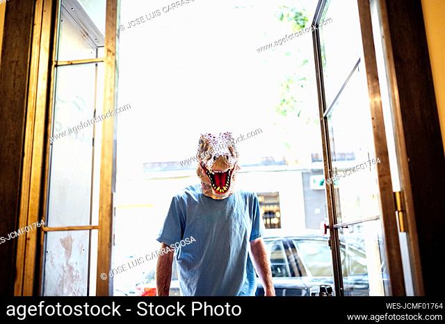 Mid adult man wearing dinosaur mask entering in coffee shop
