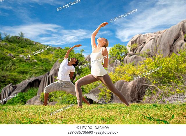 fitness, sport, people and healthy lifestyle concept - couple doing yoga in warrior pose on beach over natural background