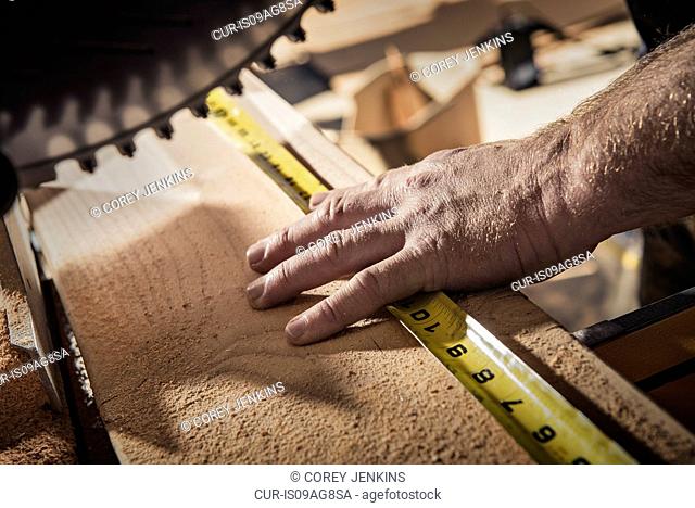 Close up of male carpenter using tape measure in workshop