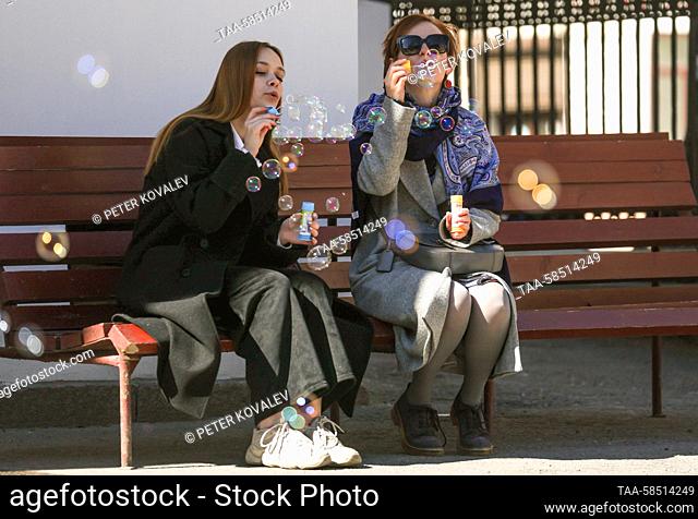 RUSSIA, ST PETERSBURG - APRIL 19, 2023: Girls blow soap bubbles sitting on a bench. Peter Kovalev/TASS