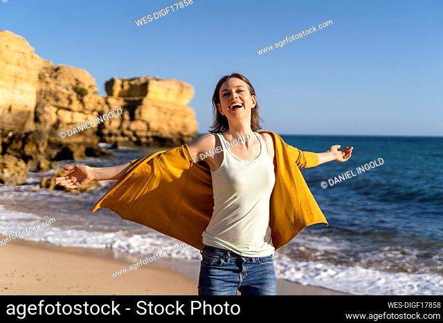 Happy woman with arms outstretched enjoying at beach on sunny day