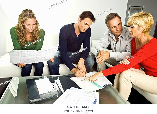 Young couple signing document with mature couple at home