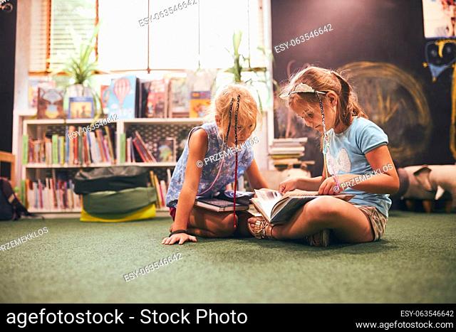 Two primary schoolgirls doing homework in school library. Students learning from books. Pupils having fun in library. Back to school