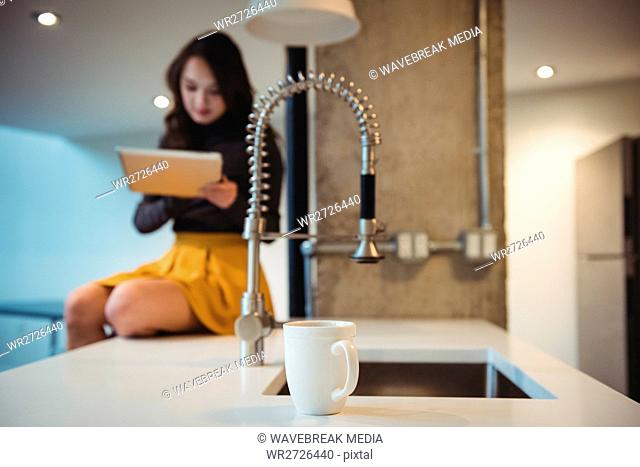 Woman sitting on kitchen worktop using digital tablet