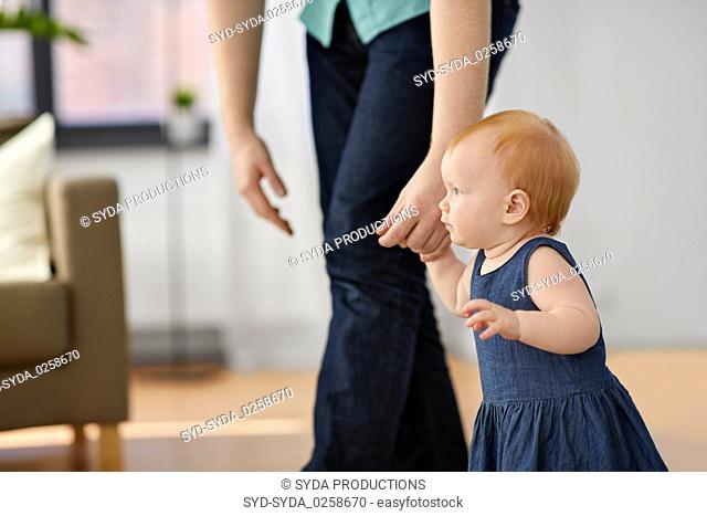 baby girl walking with father help at home