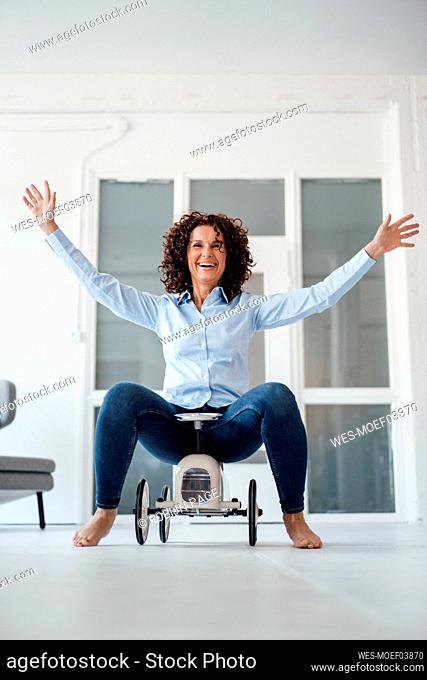 Cheerful businesswoman on toy car having fun at office