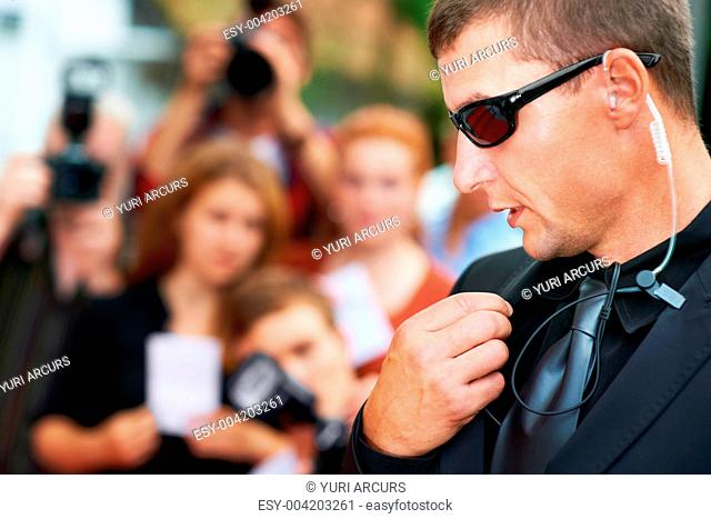 A security guard wearing dark glasses talking into his radio on the red carpet at a movie premiere - Copyspace
