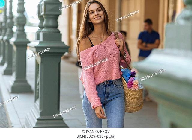 Sonriente mujer caucásica llevando flores en la acera