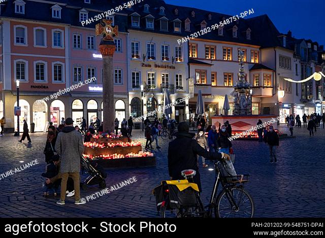 02 December 2020, Rhineland-Palatinate, Trier: In the evening, people commemorate the victims of an amok drive at the market cross and the Petrusbrunnen and put...