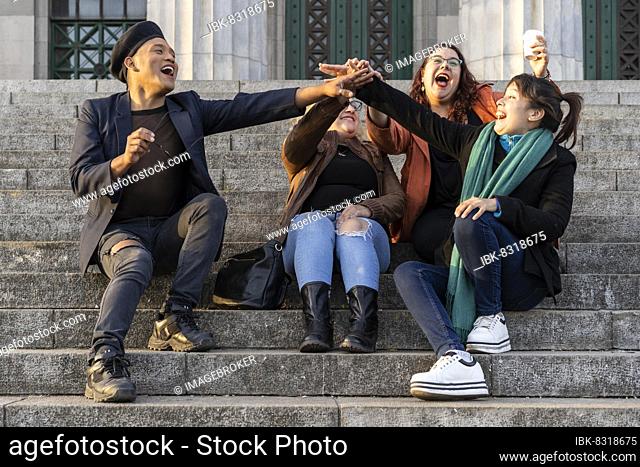 Multi ethnic group of friends sitting on some stairs having a good time chatting and laughing