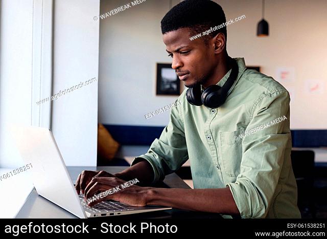 Determined african american young businessman with headphones working on laptop in creative office