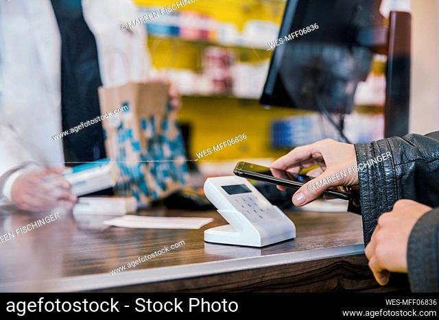 Hand of customer with mobile phone at checkout counter in chemist shop
