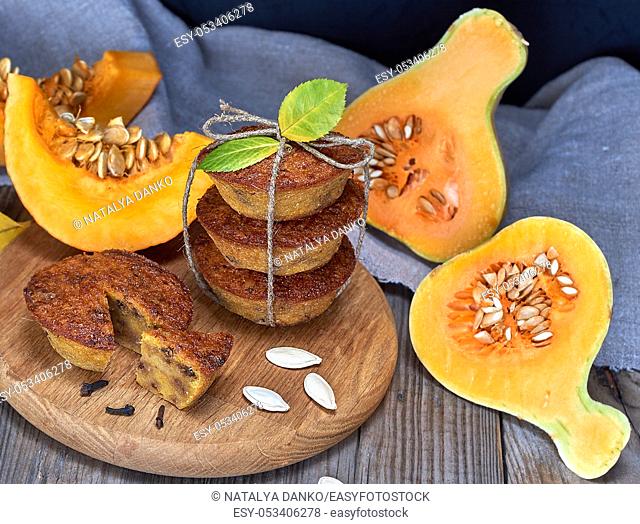 stack of muffins with a pumpkin on a round wooden board and fresh pieces of pumpkin