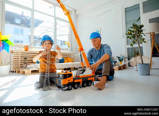 Boy imitating as engineer attaching electricity pylon model to toy crane with grandfather at home