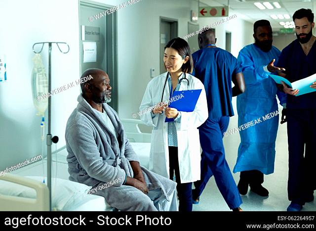 Happy asian female doctor and senior african american male patient talking in hospital corridor