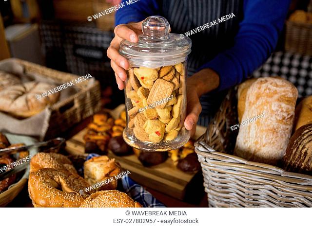Mid section of staff holding glass jar of cookies at counter