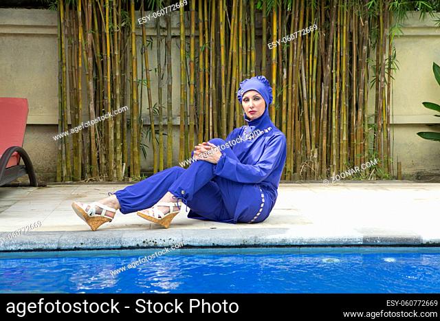 attractive woman in a Muslim swimwear burkini on a pool side in a tropical garden