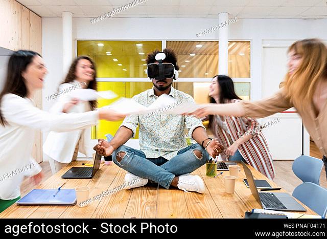 Businessman sitting on desk in conference room in office wearing VR goggles