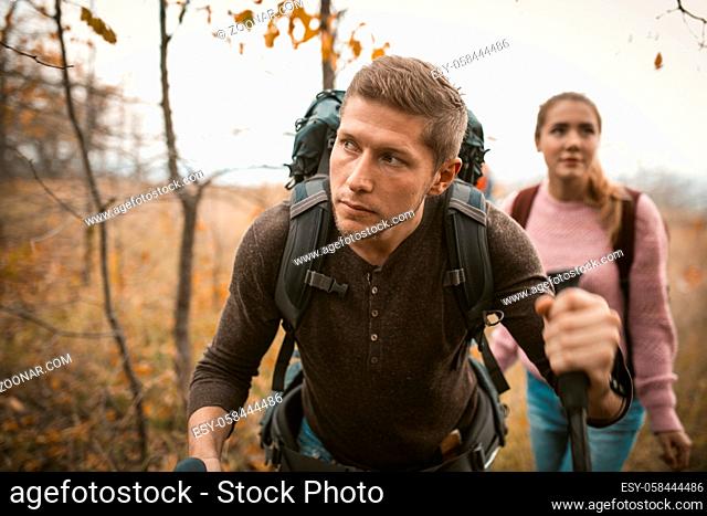 Young Caucasian Man And Woman Are Hiking In Autumn Nature Outdoors, Traveling Couple With Backpacks Makes Their Way Through Bush, Hiking Concept
