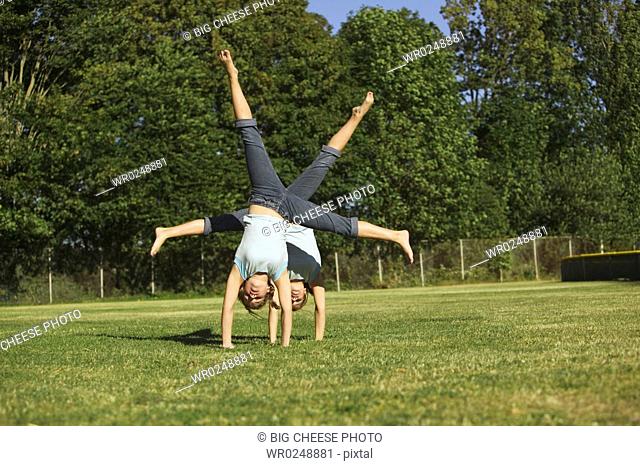 Twin teenage girls turning cartwheels in park