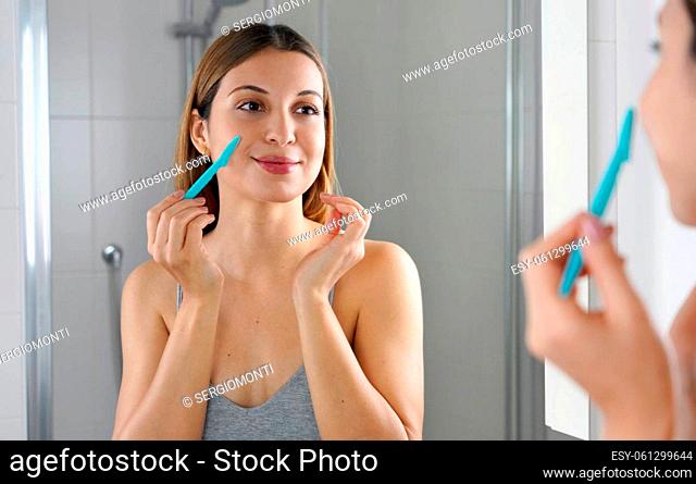 Beauty woman shaving her face by razor at home. Pretty girl using razor on bathroom. Facial hair removal